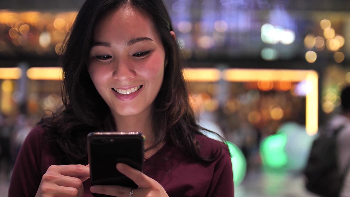 亚洲年轻女子晚上在城市里用漂亮的Bokeh智能手机