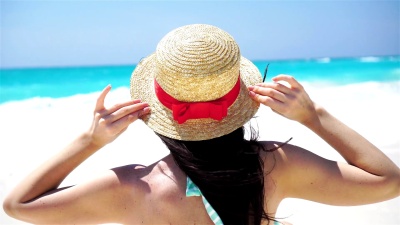 白色海滩上的夏日假期戴着帽子的美女的背影。