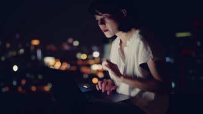 年轻的亚洲女人坐在阳台上用笔记本电脑工作