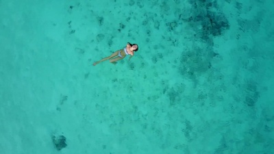 鸟瞰一位穿着比基尼的迷人女子漂浮在水晶般清澈的大海中。漂亮的女孩在印度洋游泳