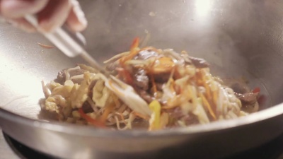 厨师在炒锅里煮肉蔬菜面条的特写镜头