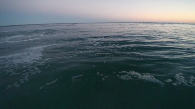 年轻的男子和十几岁的女孩在日落时在海洋中游泳，在海浪中被海浪击中。美国纽约州长岛汉普顿海滩。