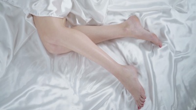卧室里的美女躺在床上。白色床单上的女人腿特写镜头