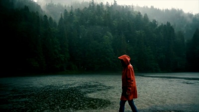 穿着雨衣的女人在倾盆大雨中站在湖边