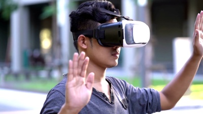 亚洲男子在花园戴着VR头盔。用手做手势。