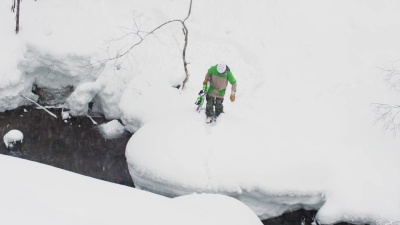 滑雪者在日本深山粉雪中危险地跳过河流