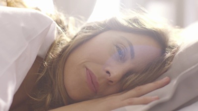 人们醒来-年轻女子在阳光明媚的早晨睁开眼睛