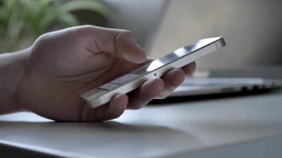 男性的手在martphone上滚动新闻线，背景中的笔记本电脑每秒60帧