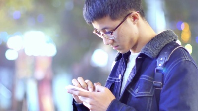 亚洲男学生晚上在校园里拿着手机