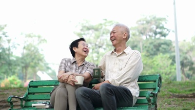 慢动作快乐的亚洲老年夫妇坐在早晨公园喝茶，喝咖啡。交谈和表达爱意