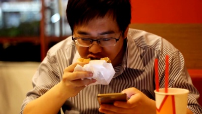 男人一边吃汉堡一边用智能手机