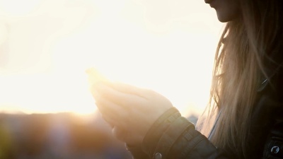 特写镜头，女性手持智能手机在街上。日落时使用无线技术的女人