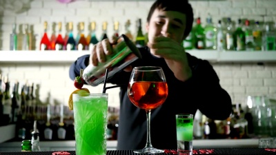 酒吧里的酒保在工作场所用威士忌和柠檬把冰块从摇壶里撒到鸡尾酒里