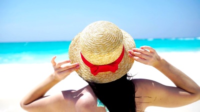 白色海滩上的夏日假期戴着帽子的美女的背影。