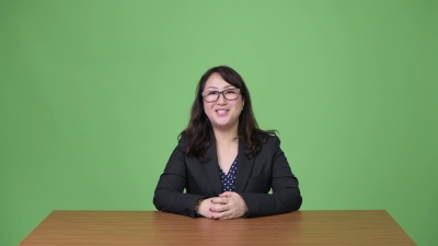 坐在办公桌后对着镜头说话的成熟美丽的亚洲女商人