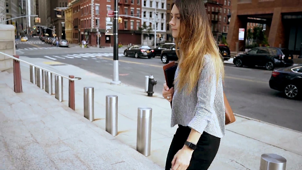 年轻美丽的女商人走在美国纽约金融区，看着手表。慢动作