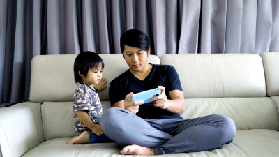  年轻的亚洲男子和男婴在智能手机上玩游戏。