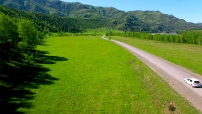 在丘陵和草地上蜿蜒的道路上飞过汽车。下部农村公路