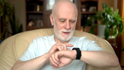 帅气，笑容满面的老人坐在家里的椅子上。使用智能手表，发送消息
