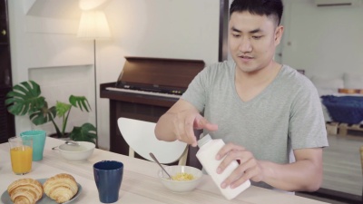快乐的亚洲男人吃早餐，牛奶里的谷类食品，面包和早上醒来后喝橙汁。生活方式男人在家吃饭的概念。