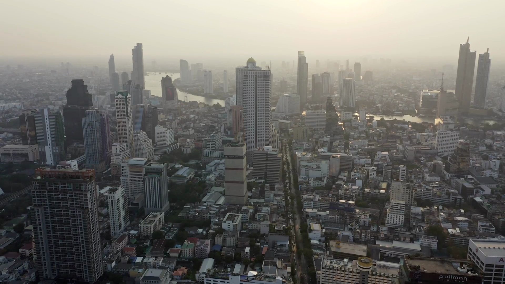 俯瞰泰国曼谷城市，主要商业区有湄南河和高层办公楼，背景是日落。