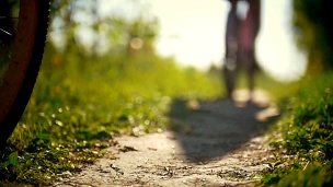 在一个阳光明媚的日子，骑自行车的人的腿，两个年轻的女孩在绿色的森林中的一条小路上经过