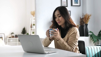 年轻的亚洲女性喝咖啡，使用笔记本电脑，在家工作