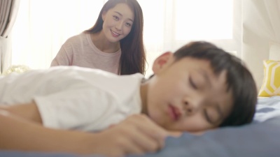 年轻的亚裔母亲微笑的特写镜头&早上叫醒她的儿子