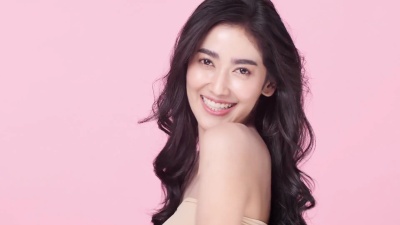 美丽的亚洲女人肖像。美丽的女人抚摸着她的脸。具有青春和护肤理念的人。在粉红色背景上隔离。