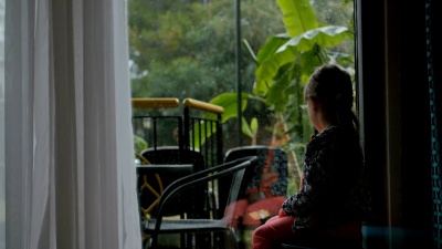 小女孩坐在后院里从里面看。想玩但外面下大雨