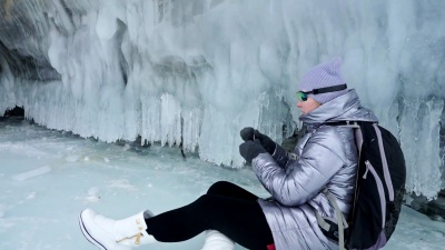 女人在贝加尔湖的冰上旅行。冬岛之旅。女孩正走在冰山脚下。旅行者看着美丽的冰窟。极限跋涉和步行。背包客在大自然中休息。