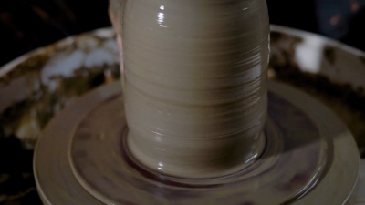 粘土花瓶的特写镜头，母子在手的帮助下形成了产品的形状，罐子站在陶工的轮子上
