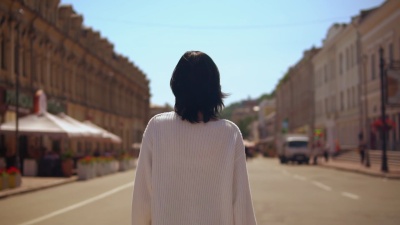穿着白色套头衫和黑色裙子的深色女性步行