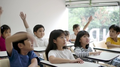 一群快乐的亚洲小学生在课堂上举起手臂回答老师的问题。幼儿园学前概念。