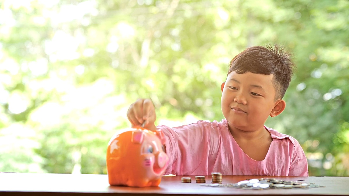 带着快乐微笑的亚洲男孩有趣地把硬币放进存钱罐，慢动作。bokeh背景。存钱，为将来募集钱。