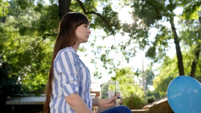 口渴的女人喝着清凉的水，对着大自然公园里的背景树微笑