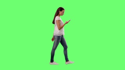 休闲的年轻布鲁内特女孩在背景中的模拟绿色屏幕上在智能手机上行走和交谈。
