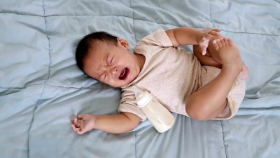 小男孩抱着奶瓶在床上哭。