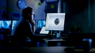 年轻的胡须工程师在工业涡轮的3D模型上工作。夜深人静的时候，他是黑暗办公室里唯一剩下的人。