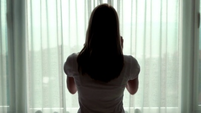 穿着白色T恤的女人揭开窗帘，看着窗外。享受外面的海景