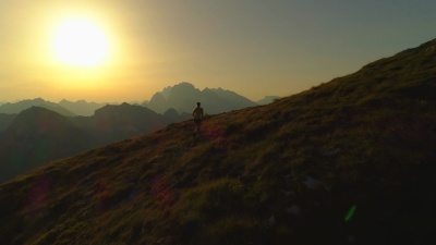 空中 年轻女子在日落时攀登并到达山顶的剪影。