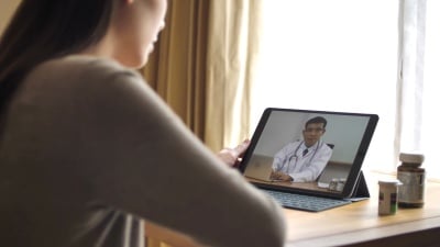 女性患者在家用数字平板电脑与资深医生交谈