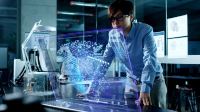 亚洲神经网络工程师使用透明全息显示的现代计算机。显示器显示交互式人工智能界面。在现代玻璃和混凝土办公室拍摄。