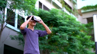 亚洲男子在花园戴着VR头盔。用手做手势。