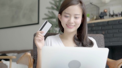 美丽的肖像年轻的亚洲女性用信用卡在线购物，坐在家里客厅的笔记本电脑上，女孩与客户在线购买付款，生活方式的概念。