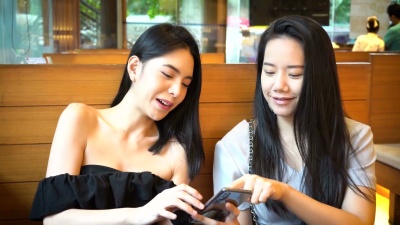 两个亚洲女性朋友用手机一起笑。女性在日本餐厅享受美好时光