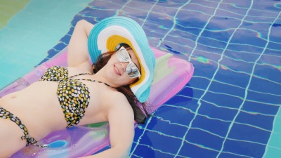 一位戴着太阳镜的年轻女子在充气床垫上晒黑，在游泳池里游泳