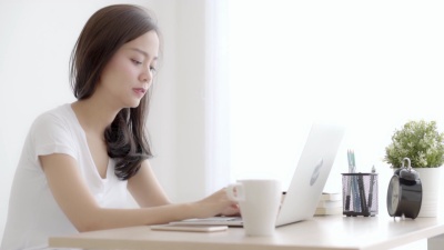 美丽年轻的自由亚洲女性微笑着在笔记本电脑上工作，在办公桌上与专业的女孩交谈移动智能手机，使用笔记本电脑，商业和生活方式的概念。