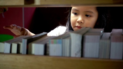 可爱的亚洲小女孩在图书馆的书架上找到一本书