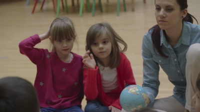   幼儿园老师和孩子们坐在教室的地板上。